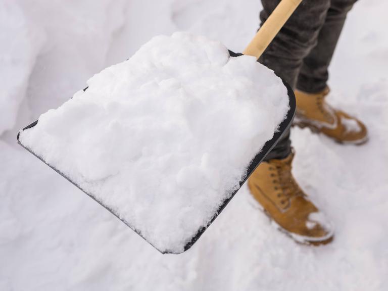 Nahaufnahme einer Person, die Schnee schaufelt.