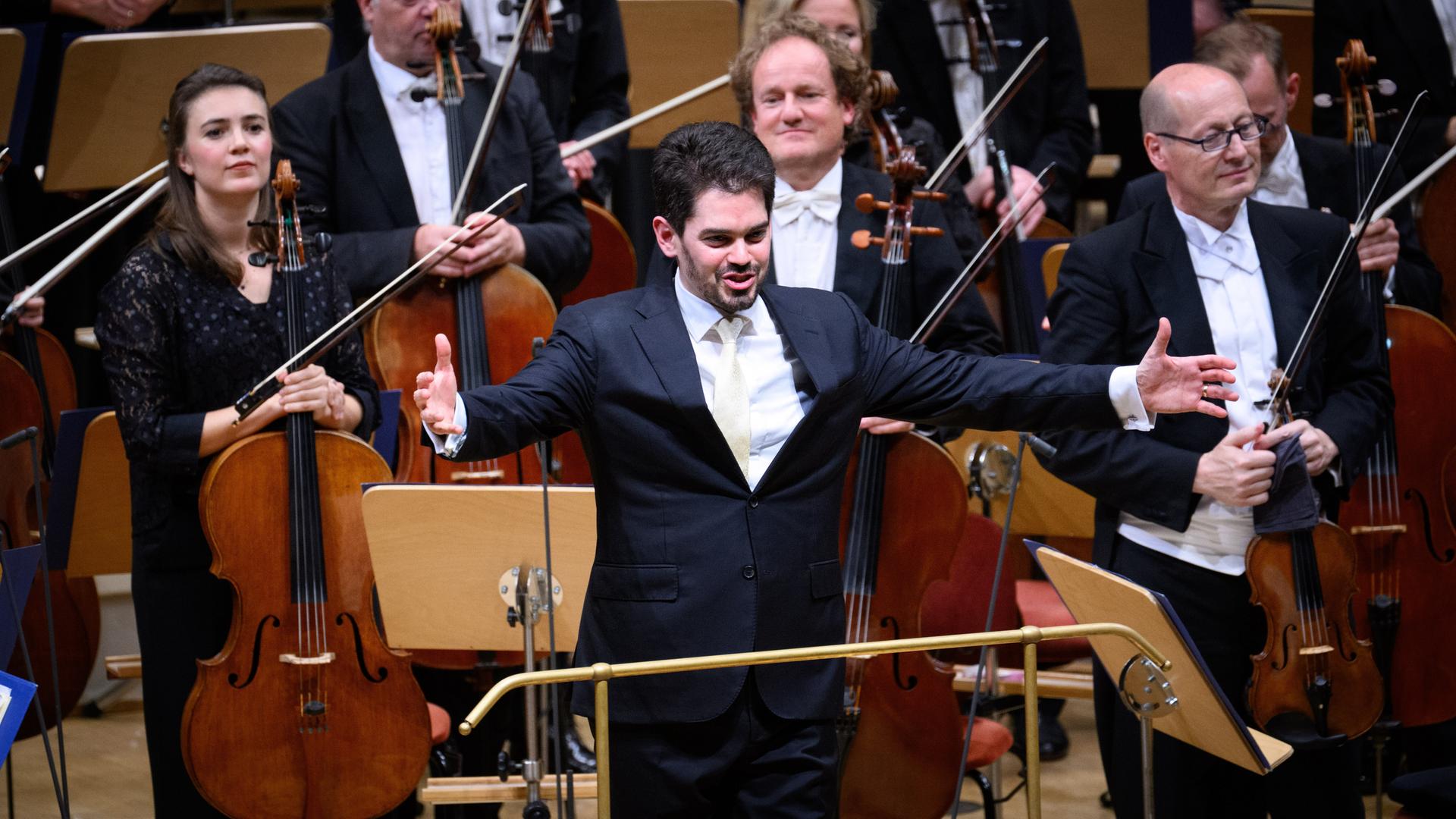 Der zukünftige Chefdirigenten der Münchner Philharmoniker, Lahav Shani, nimmt beim Musikfest Berlin den Applaus entgegen. Er steht vor den Cellisten und Violinisten und breitet die Arme aus.