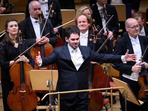 Der zukünftige Chefdirigenten der Münchner Philharmoniker, Lahav Shani, nimmt beim Musikfest Berlin den Applaus entgegen. Er steht vor den Cellisten und Violinisten und breitet die Arme aus.