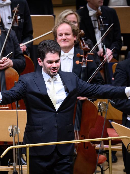 Der zukünftige Chefdirigenten der Münchner Philharmoniker, Lahav Shani, nimmt beim Musikfest Berlin den Applaus entgegen. Er steht vor den Cellisten und Violinisten und breitet die Arme aus.
