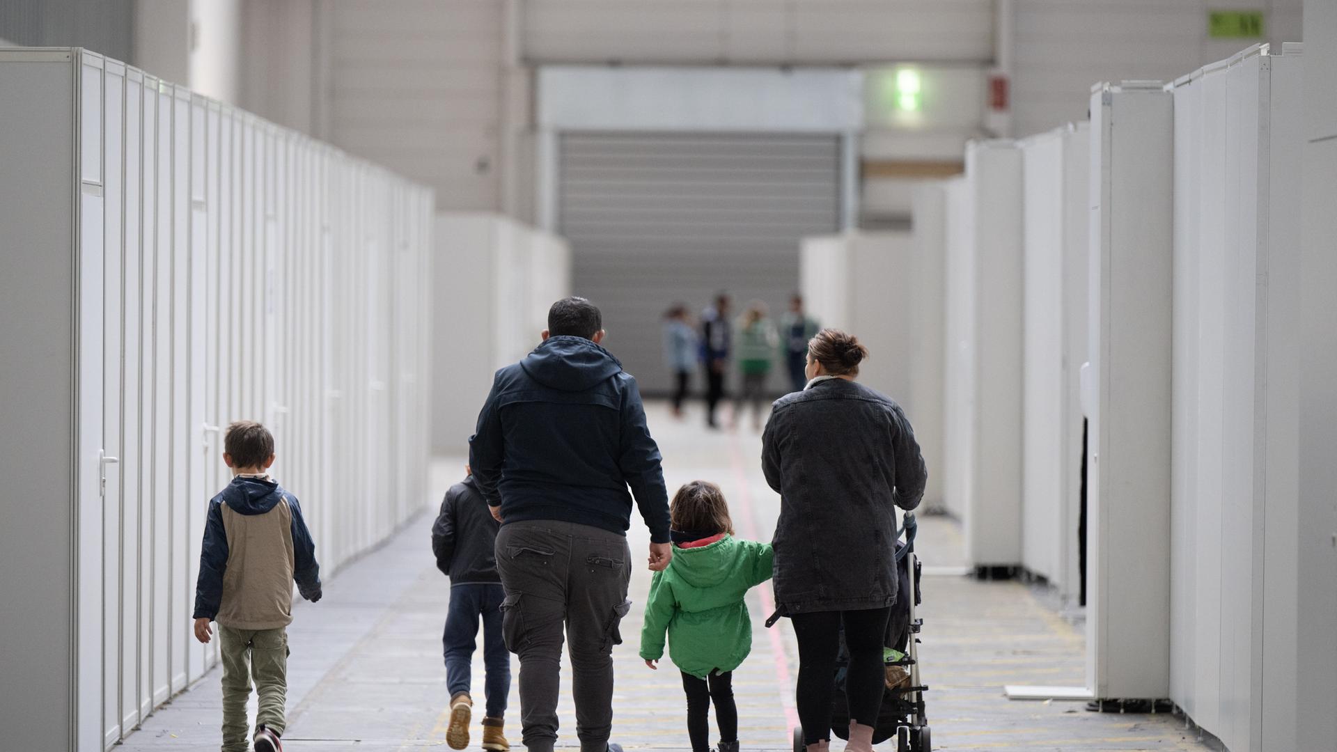 Eine Familie mit kleinen Kindern geht durch zu einer Massenunterkunft umfunktionierten Messehalle in Frankfurt.