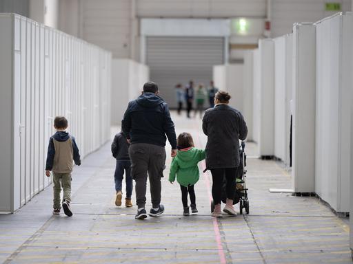 Eine Familie mit kleinen Kindern geht durch zu einer Massenunterkunft umfunktionierten Messehalle in Frankfurt.