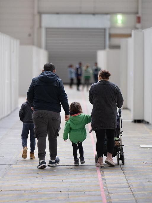 Eine Familie mit kleinen Kindern geht durch zu einer Massenunterkunft umfunktionierten Messehalle in Frankfurt.