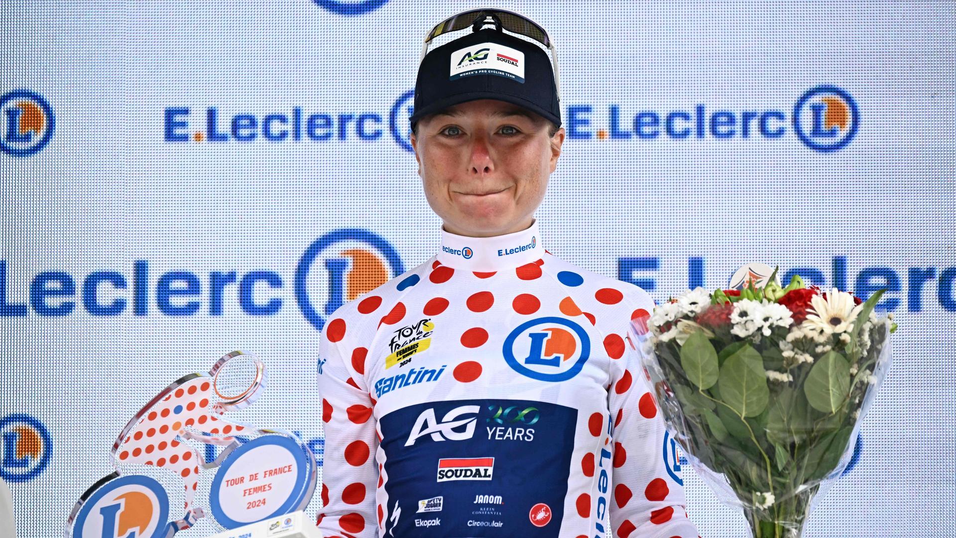 Die Belgierin Justine Ghekiere, die das gepunktete Trikot der besten Bergfahrerin trägt, jubelt auf dem Podium, nachdem sie die 7. Etappe der Tour de France Femmes gewonnen hat.