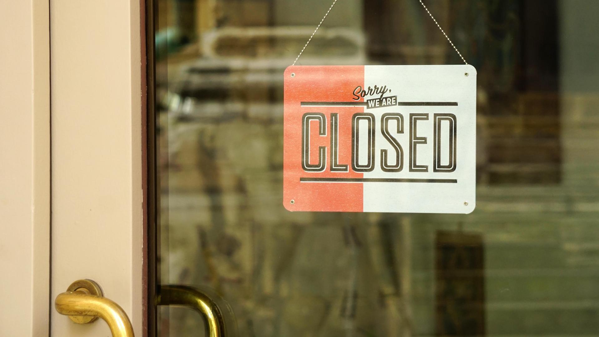 In einer verglasten, geschlossenen Ladentür hängt von innen ein Schild mit der Aufschrift "Schild, sorry we are closed".
In einer verglasten, geschlossenen Ladentür hängt von innen ein Schild mit der Aufschrift "Schild, sorry we are closed".