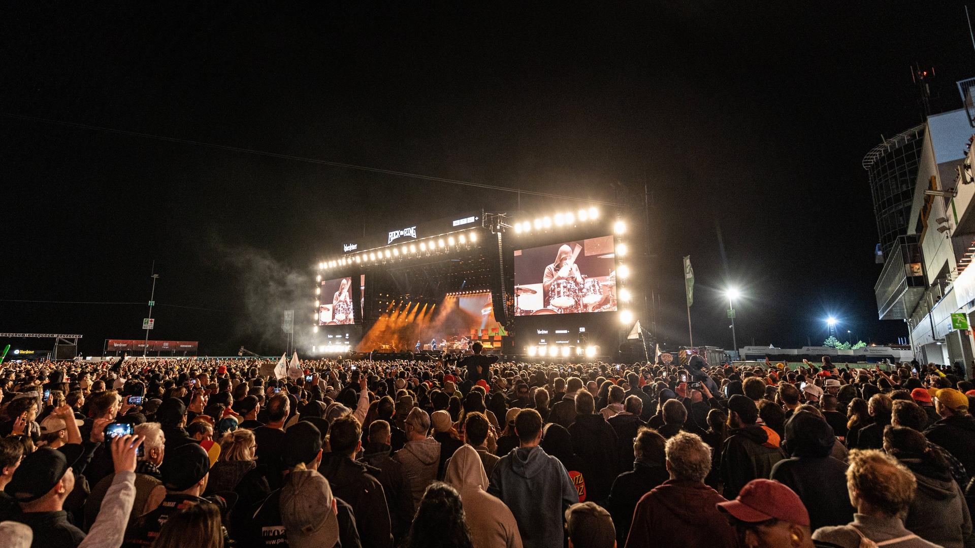 Ein voll besetztes Zuschauerfeld vor einer hell erleuchteten Festivalbühne in der Nacht. Ein voll besetztes Zuschauerfeld vor einer hell erleuchteten Festivalbühne in der Nacht.