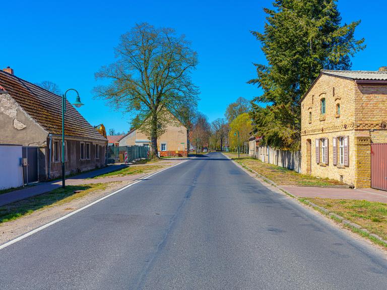 Eine Landstraße, die durch ein Dorf führt. Rechts und links sind alte Häuser zu sehen - Beispiele für historische Dorfarchitektur mit denkmalgeschützte Fassaden.