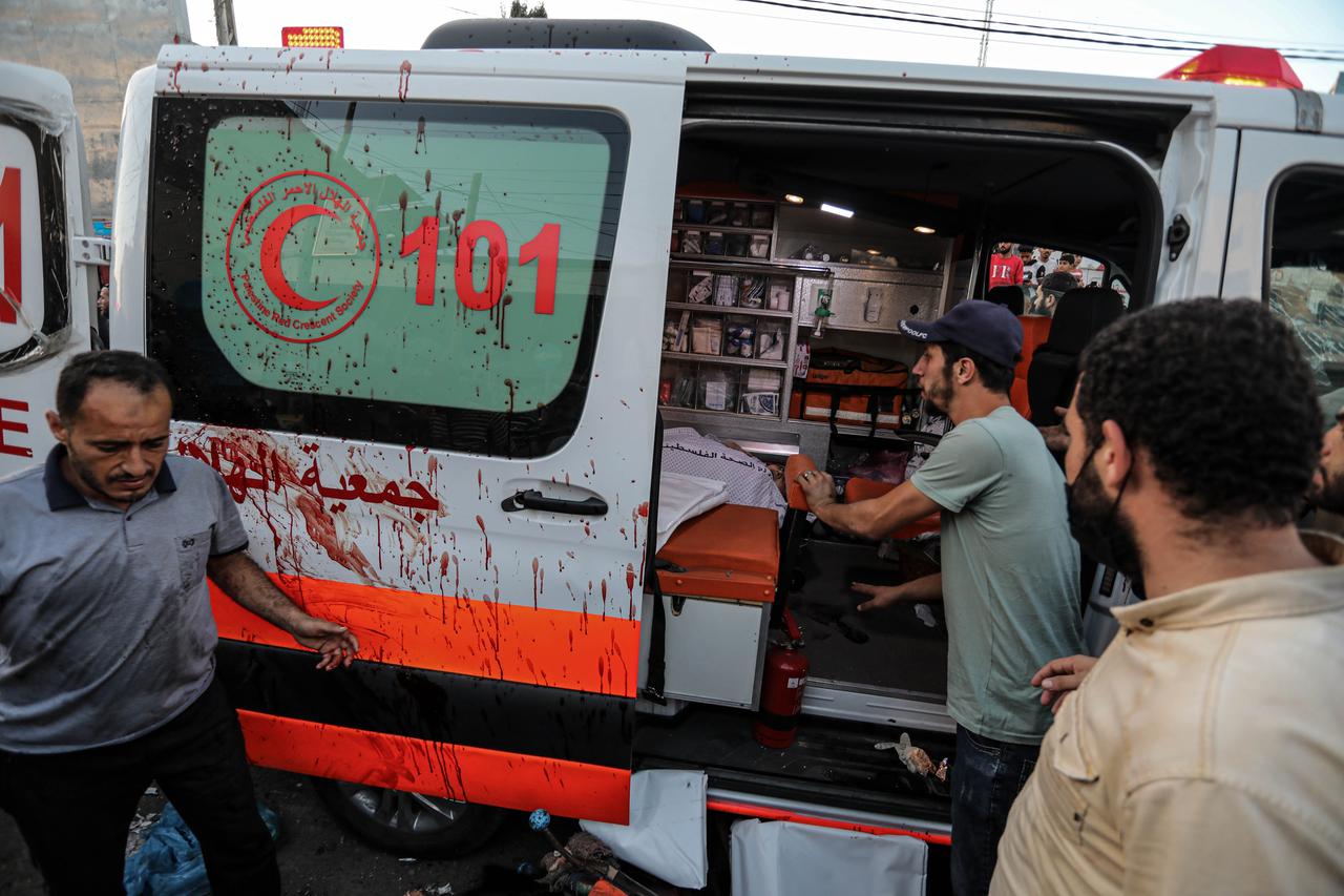 Die seitliche Schiebetür des Krankenwagens des Roten Halbmonds ist offen und voller Blutspritzer. Drei Palästinenser stehen davor.