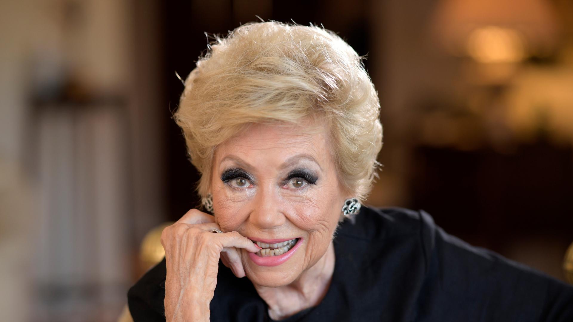 Mitzi Gaynor sitzt in einem Stuhl. Sie hält eine Hand an ihr Kinn und hat den kleinen Finger zwischen ihren Lippen. Mitzi Gaynor sitzt in einem Stuhl. Sie hält eine Hand an ihr Kinn und hat den kleinen Finger zwischen ihren Lippen.