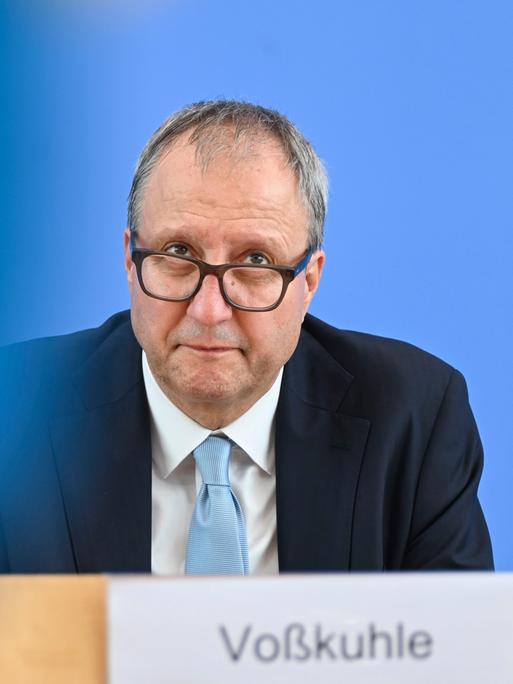 Andreas Voßkuhle blickt bei einer Pressekonferenz über seine Brillengläser nach oben. Er trägt eine hellblaue Krawatte zum dunkelblauen Anzug.