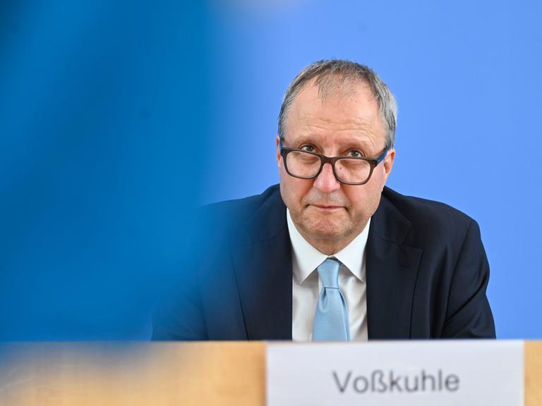 Andreas Voßkuhle blickt bei einer Pressekonferenz über seine Brillengläser nach oben. Er trägt eine hellblaue Krawatte zum dunkelblauen Anzug.