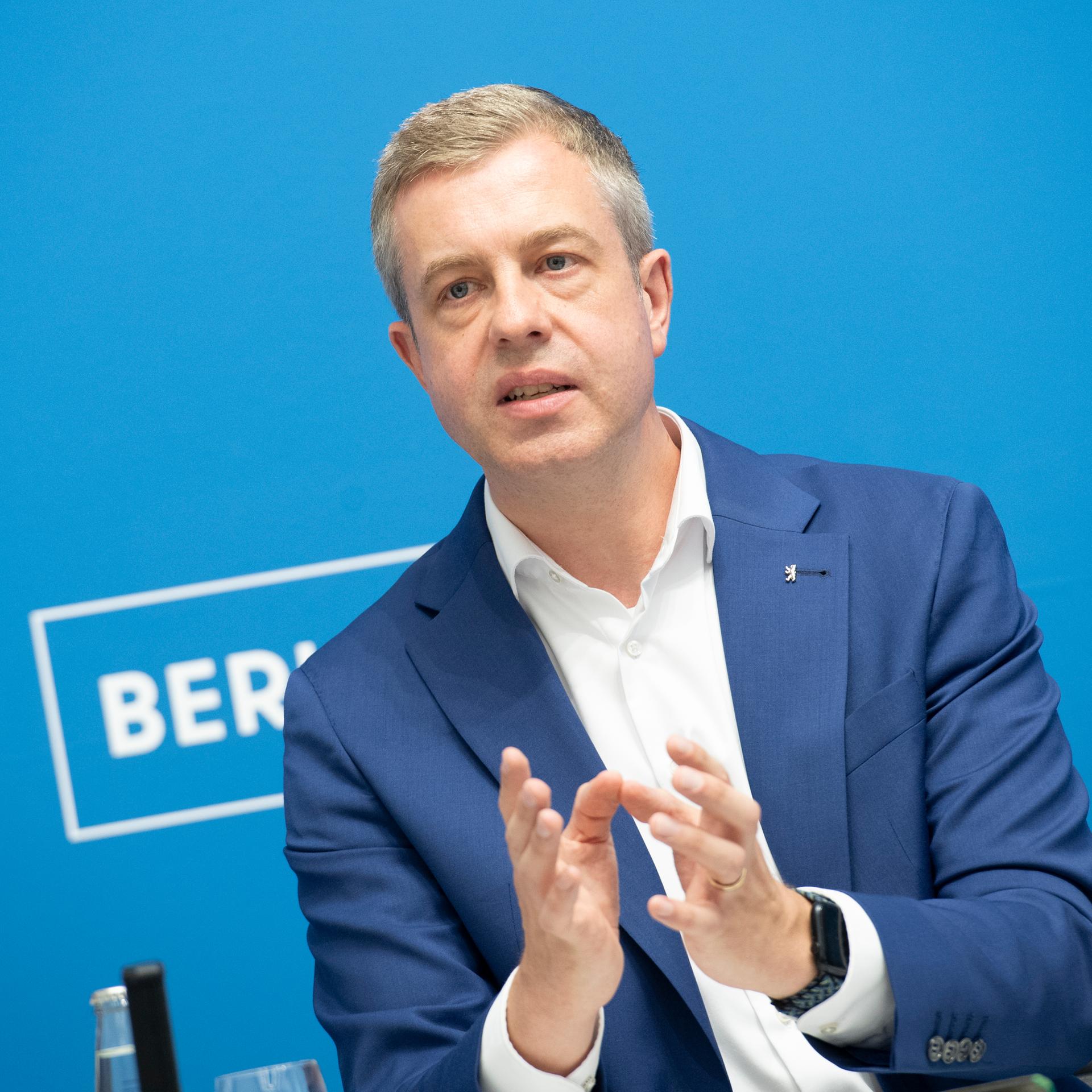 Berlins Finanzsenator Stefan Evers (CDU) in weißem Hemd und blauem Jacket vor hellblauem Hintergrund. 