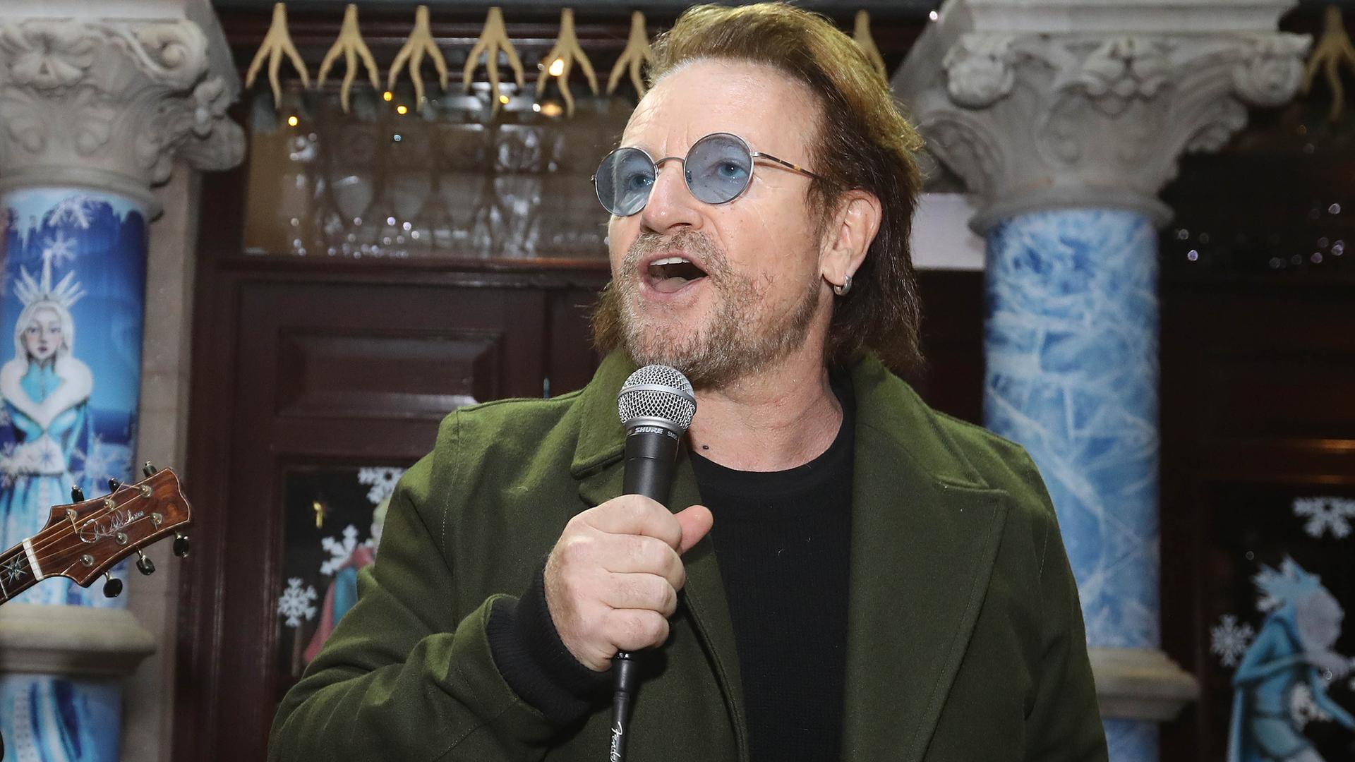 Der irische Sänger und Popstar Bono singt in ein Mikrofon. Er hat einen Drei-Tage-Bart und trägt eine Brille mit bläulich getönten Gläsern.