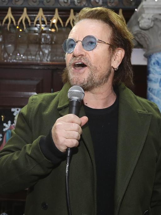 Der irische Sänger und Popstar Bono singt in ein Mikrofon. Er hat einen Drei-Tage-Bart und trägt eine Brille mit bläulich getönten Gläsern.