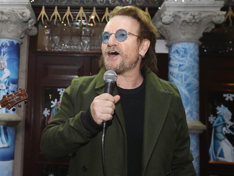 Der irische Sänger und Popstar Bono singt in ein Mikrofon. Er hat einen Drei-Tage-Bart und trägt eine Brille mit bläulich getönten Gläsern.