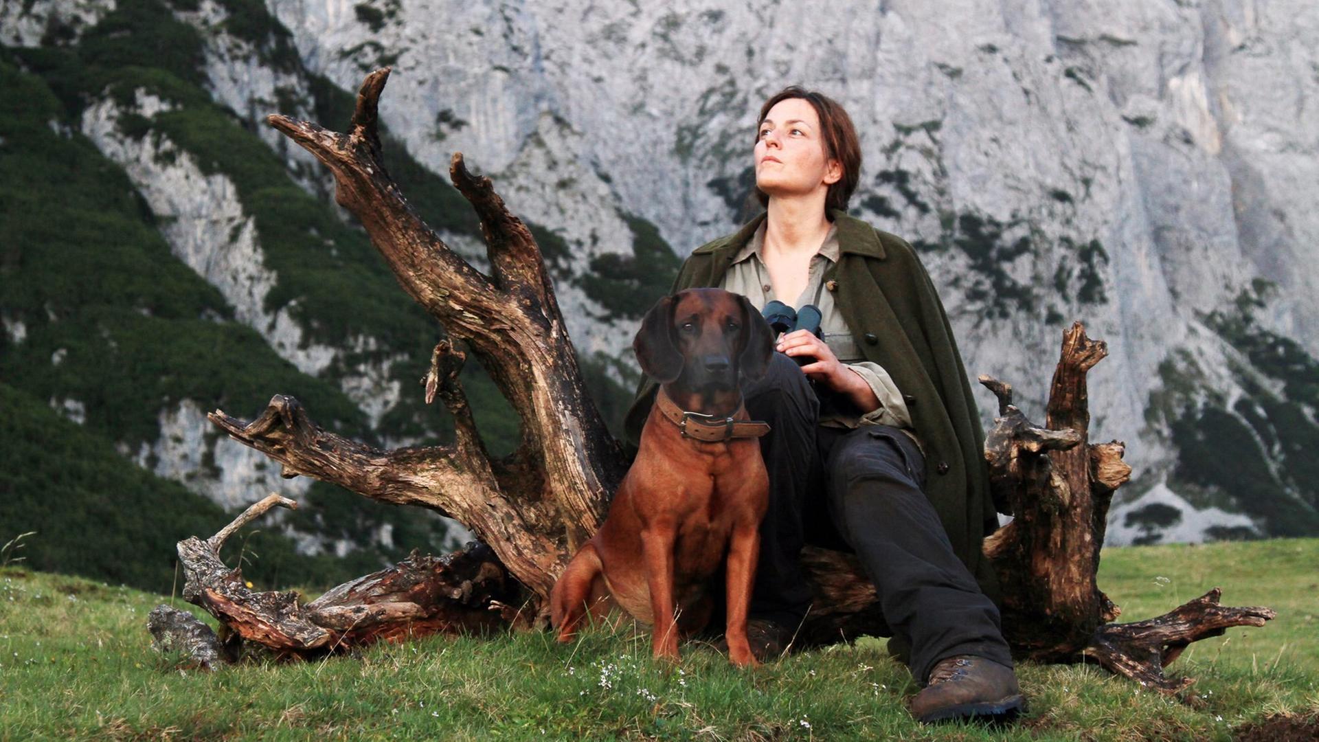 Die Schauspielerin Martina Gedeck mit einem Hund vor einer Felswand, Szene aus dem Film "Die Wand". 
