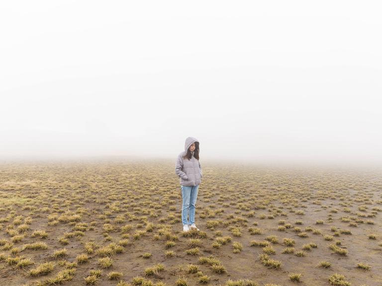 Eine junge Frau steht auf einem nebligen Feld.