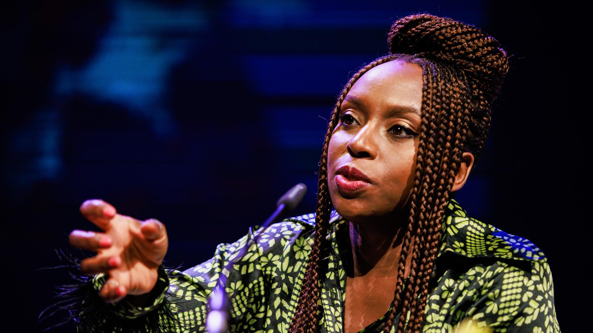 Chimamanda Ngozi Adichie spricht in ein Mikrofon und unterstreicht ihre Worte mit einer zupackenden Geste.