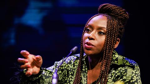 Chimamanda Ngozi Adichie spricht in ein Mikrofon und unterstreicht ihre Worte mit einer zupackenden Geste.