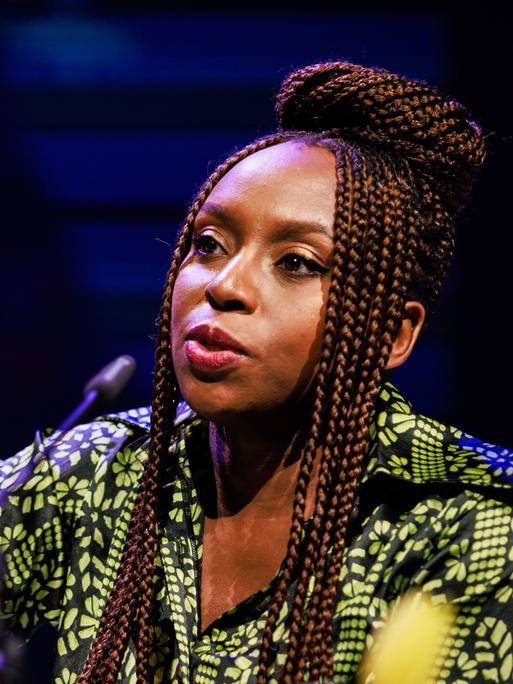 Chimamanda Ngozi Adichie spricht in ein Mikrofon und unterstreicht ihre Worte mit einer zupackenden Geste.