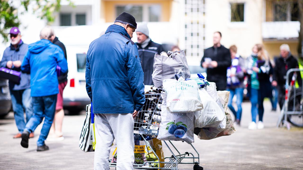 Ein mutmaßlich obdachloser Mann steht vor einem Einkaufswagen, in dem er Pfandflaschen gestapelt hat.