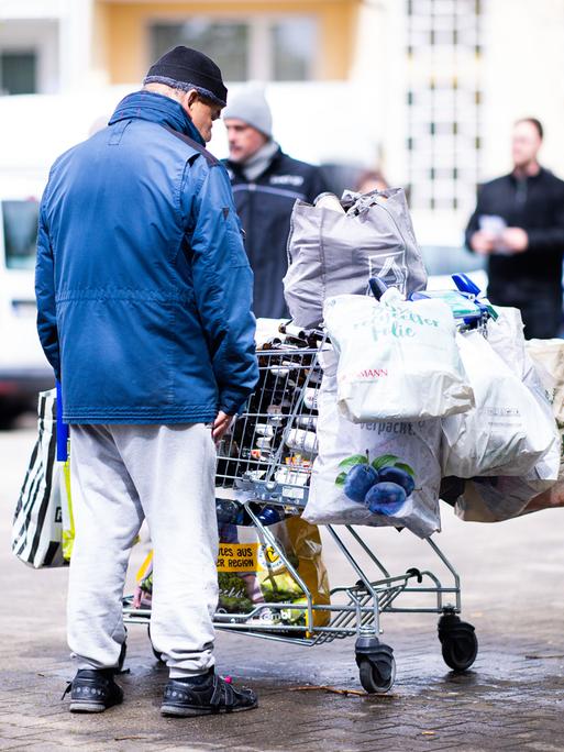 Ein mutmaßlich obdachloser Mann steht vor einem Einkaufswagen, in dem er Pfandflaschen gestapelt hat.