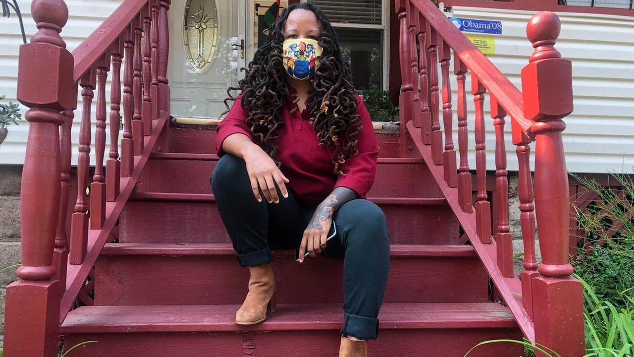 Imani Oakley sitzt auf der Treppe ihres Wohnhauses in der Stadt Montclair. Sie hat lange, schwarze Haare und trägt einen bunten Mund-Nasen-Schutz im Gesicht.