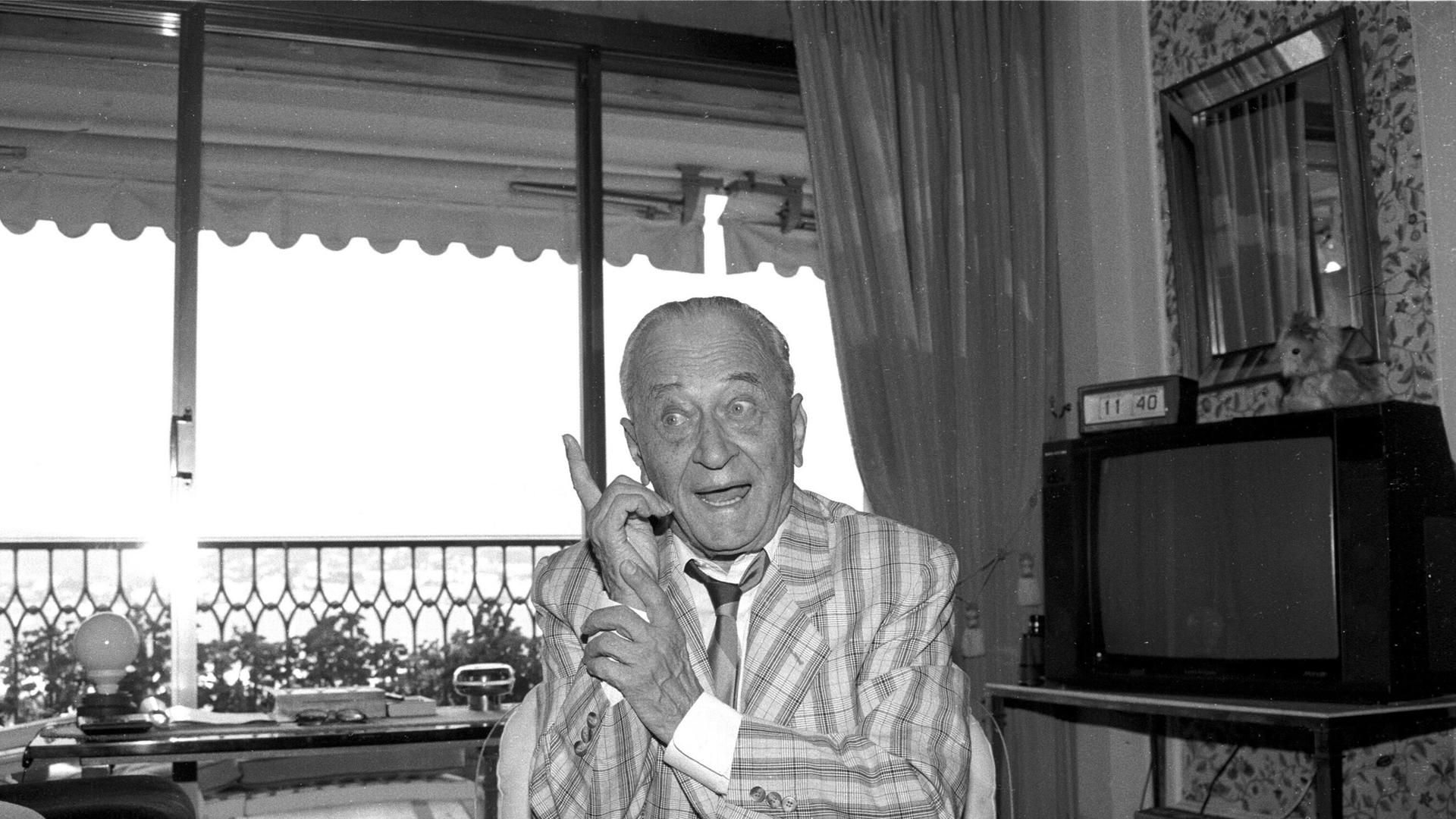 Der Journalist, Erfinder und Medienmanager Eduard Rhein Eduard Rhein sitzt in Jacket, Hemd und Krawatte in einem Wohnzimmern. Lächelnd hebt er den Zeigefiner der linken Hand. Der Journalist, Erfinder und Medienmanager Eduard Rhein Eduard Rhein sitzt in Jacket, Hemd und Krawatte in einem Wohnzimmern. Lächelnd hebt er den Zeigefiner der linken Hand.