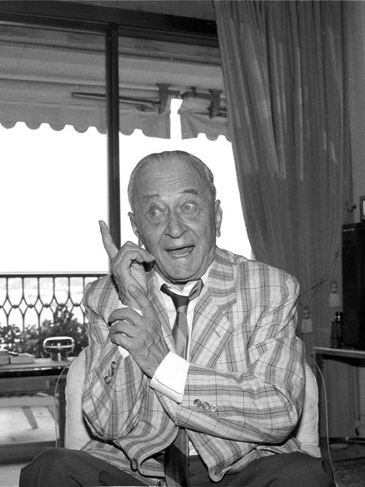 Der Journalist, Erfinder und Medienmanager Eduard Rhein Eduard Rhein sitzt in Jacket, Hemd und Krawatte in einem Wohnzimmern. Lächelnd hebt er den Zeigefiner der linken Hand. Der Journalist, Erfinder und Medienmanager Eduard Rhein Eduard Rhein sitzt in Jacket, Hemd und Krawatte in einem Wohnzimmern. Lächelnd hebt er den Zeigefiner der linken Hand.