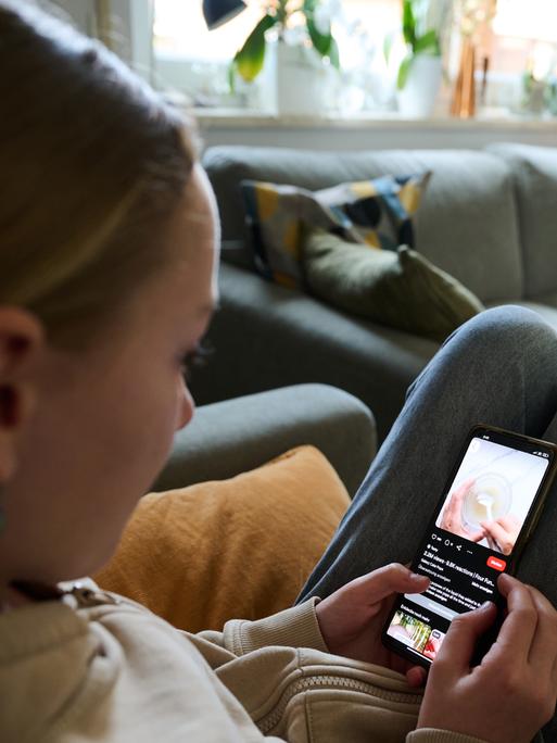 Ein Mädchen blickt auf sein Smartphone, während ein anderes Mädchen ein Buch liest.