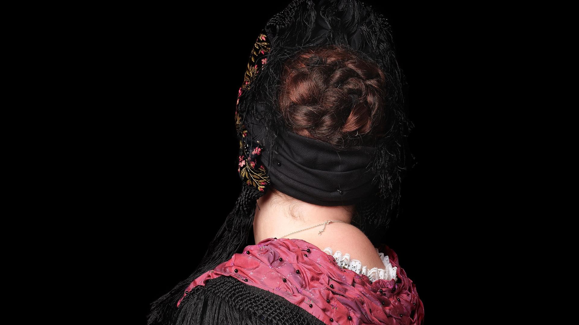 Rückenansicht einer Frau in Trachtenkleidung mit einem weißen Rock, schwarzer Bluse und verziertem rotem Schal. Rückenansicht einer Frau in Trachtenkleidung mit einem weißen Rock, schwarzer Bluse und verziertem rotem Schal.