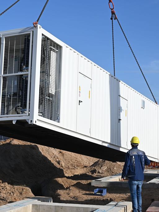 An einem fast fertigen Solarpark des Energieversorgers EnBW wird ein Batteriespeicher angeliefert. 