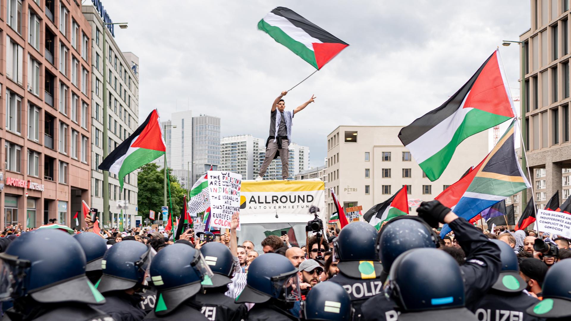 Zahlreiche Menschen ziehen in einem Demonstrationszug durch Berlin, einige schwenken palästinensische Flaggen. Im Vordergrund Polizisten mit Schutzhelmen. Zahlreiche Menschen ziehen in einem Demonstrationszug durch Berlin, einige schwenken palästinensische Flaggen. Im Vordergrund Polizisten mit Schutzhelmen.