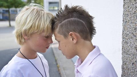 Zwei Jungs auf dem Schulhof stehen Stirn an Stirn.