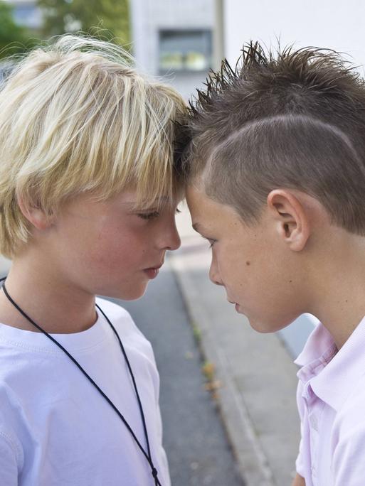 Zwei Jungs auf dem Schulhof stehen Stirn an Stirn.