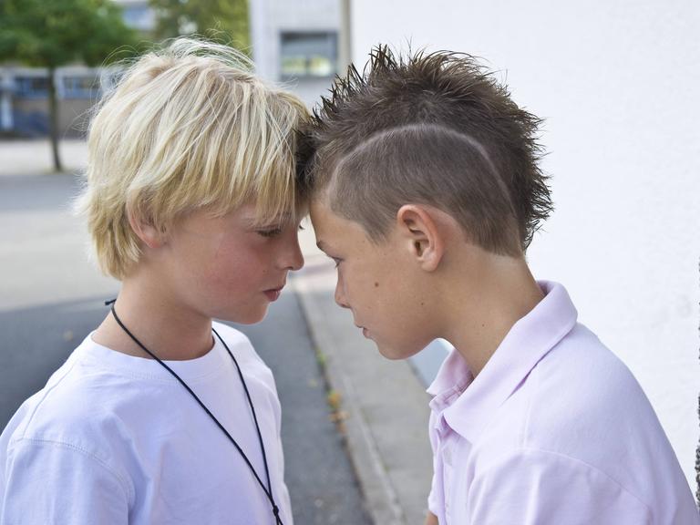Zwei Jungs auf dem Schulhof stehen Stirn an Stirn.