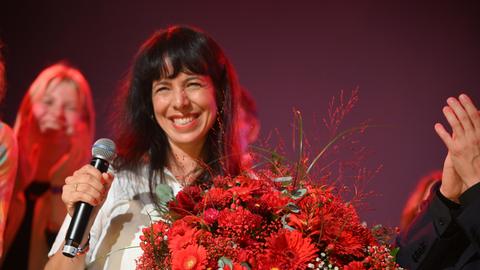 Elif Eralp steht mit einem Blumenstrauß auf der Bühne und lächelt in die Kamera.