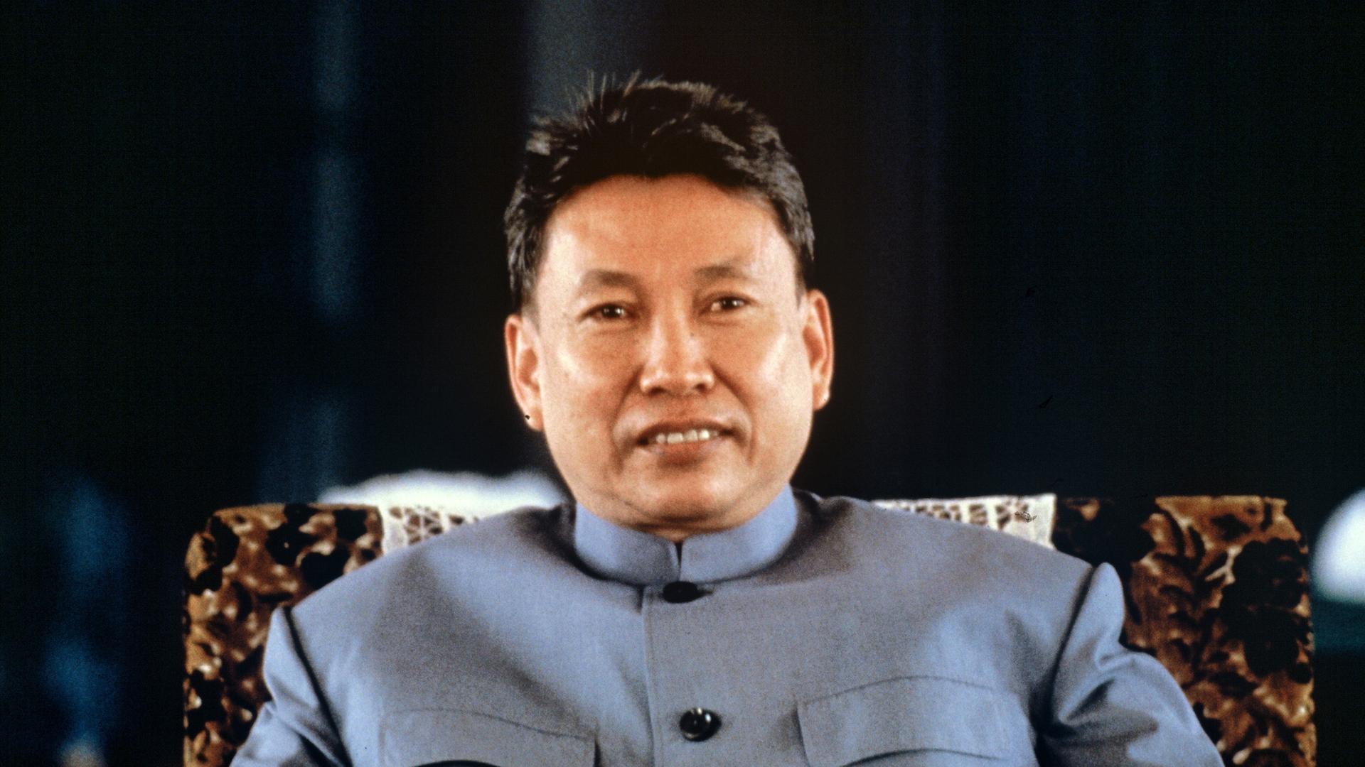 Pol Pot sitzt mit einer blauen Jacke auf einem Stuhl. Er hat eine kurze Frisur und blickt in die Kamera. Pol Pot sitzt mit einer blauen Jacke auf einem Stuhl. Er hat eine kurze Frisur und blickt in die Kamera.