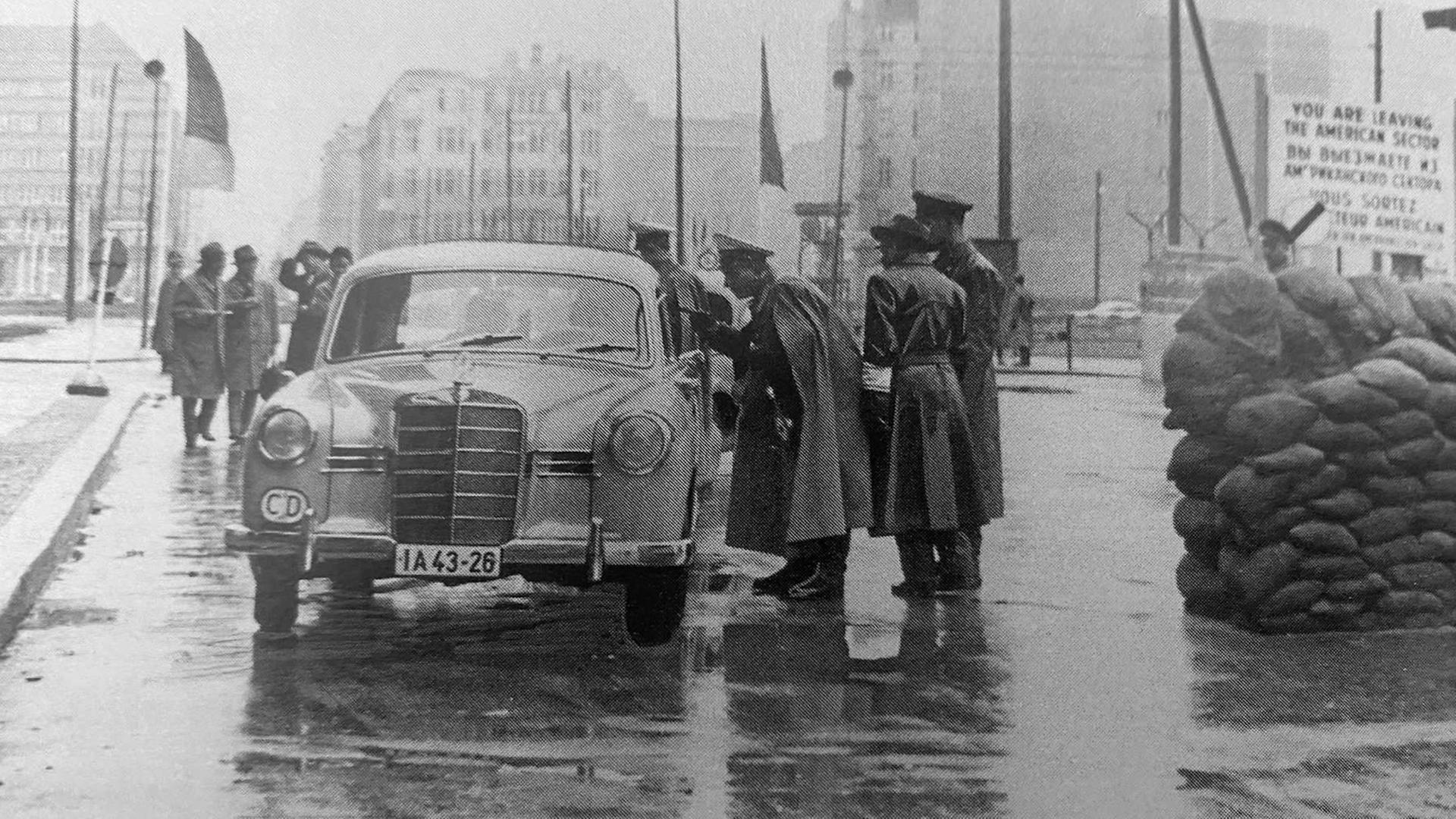 Historisches Schwarzweißfoto eines Autos, das an einem Kontrollpunkt von Polizisten umringt steht.