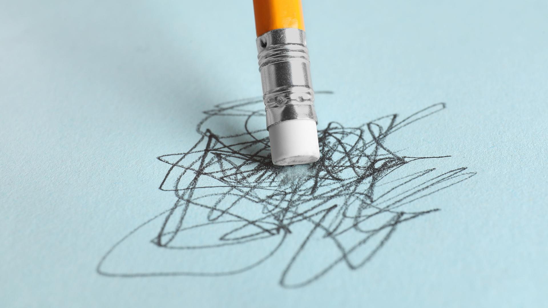 Ein Bleistift steht mit der Radiergummiseite auf einem vollgekritzelten hellblauen Blatt Papier. Ein Bleistift steht mit der Radiergummiseite auf einem vollgekritzelten hellblauen Blatt Papier.