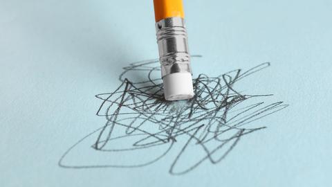 Ein Bleistift steht mit der Radiergummiseite auf einem vollgekritzelten hellblauen Blatt Papier.
