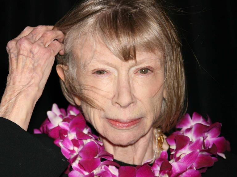 Die Publizistin Joan Didion blickt in die Kamera und schiebt sich eine Schräne aus dem Gesicht.