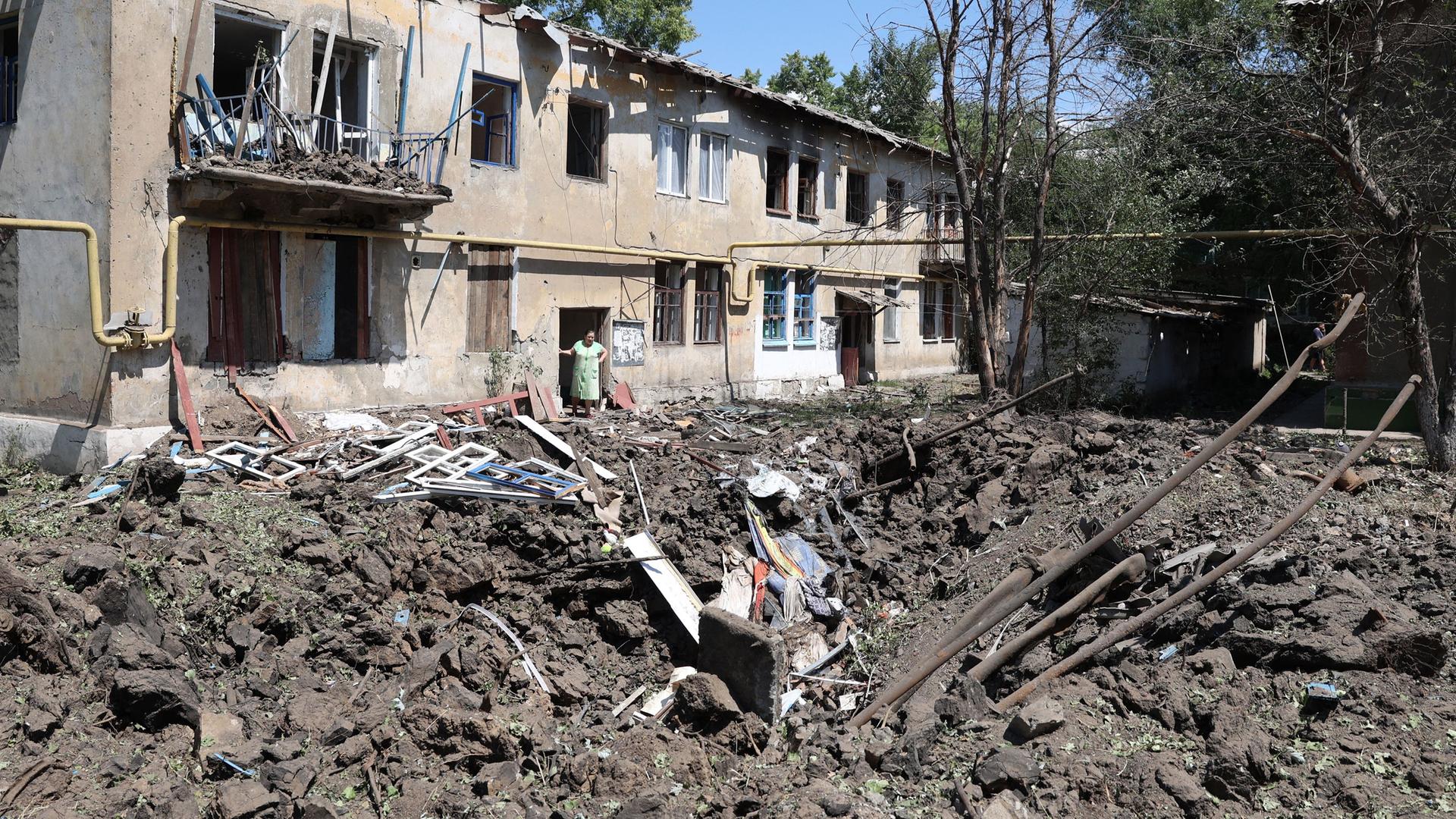 Eine Straße und ein Haus in der Donezk-Region in der Ukraine, die durch eine russische Rakete völlig zerstört sind. Eine Frau steht in einer Tür.