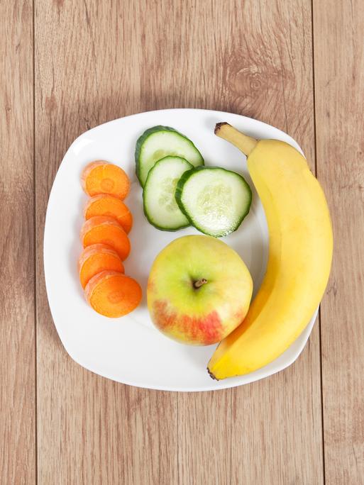 Zwei Teller: auf einem Tabletten, auf dem anderen Obst und Gemüse.