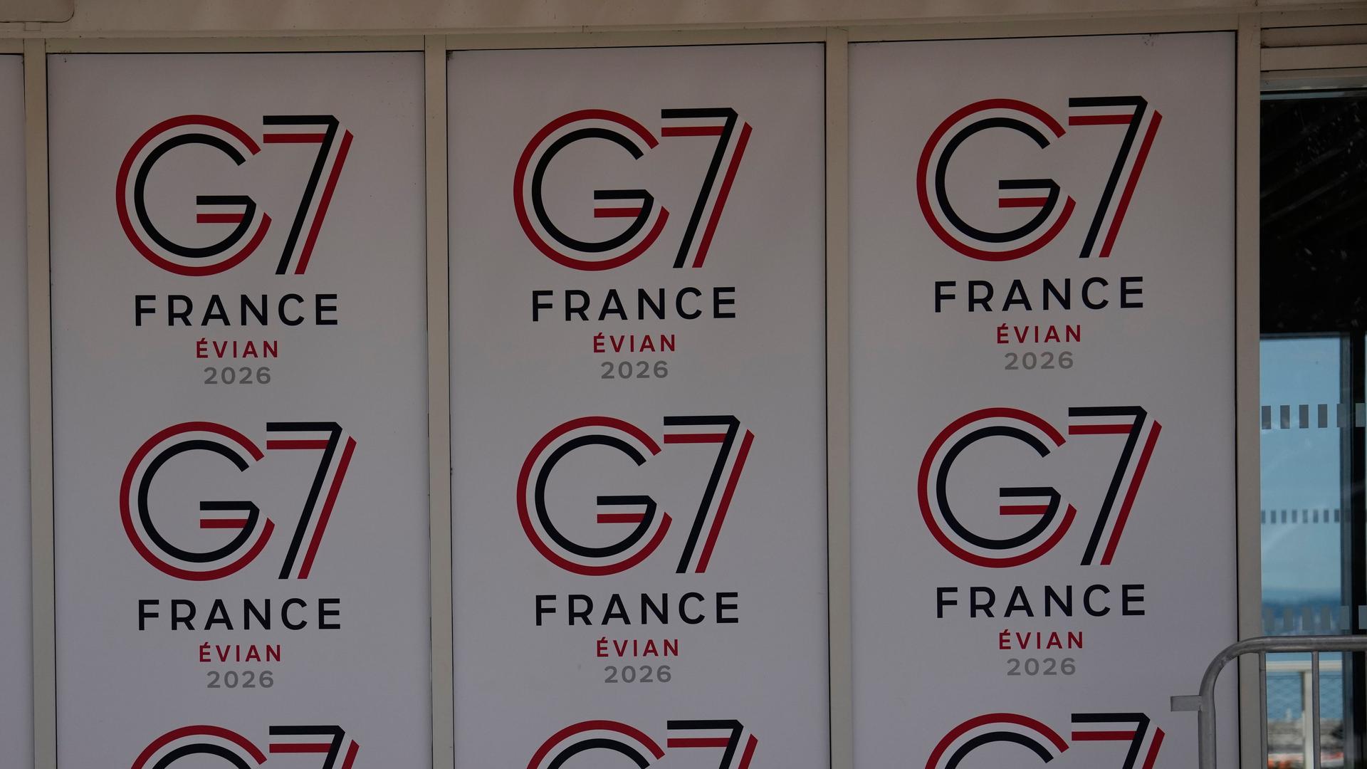 Eine Wand, auf der mehrmals das Logo des G7-Treffens zu sehen ist. In kleiner werdender Schrift steht untereinander G7, France, Evian und 2026.
