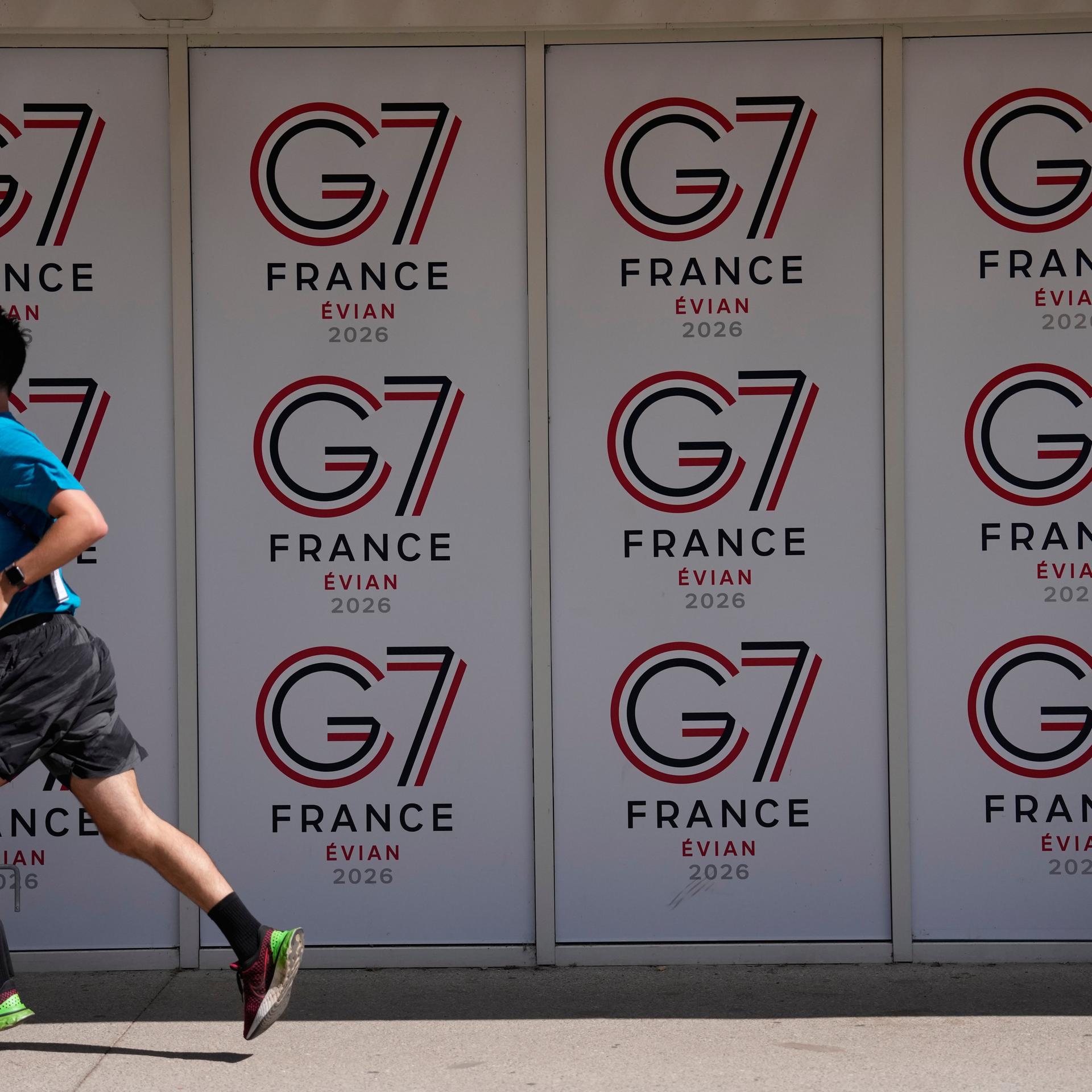 Eine Wand, auf der mehrmals das Logo des G7-Treffens zu sehen ist. In kleiner werdender Schrift steht untereinander G7, France, Evian und 2026.