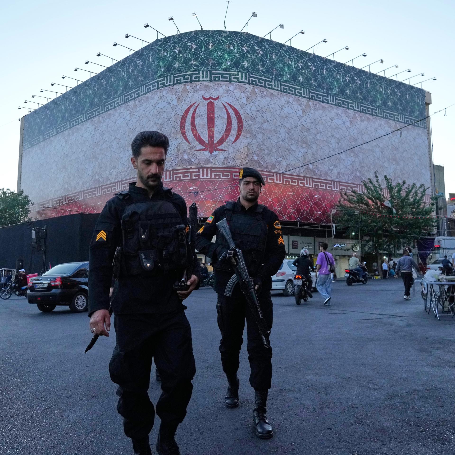 Polizisten gehen in Teheran auf dem Platz der Islamischen Revolution vor einem riesigen Banner mit der iranischen Flagge vorbei. 