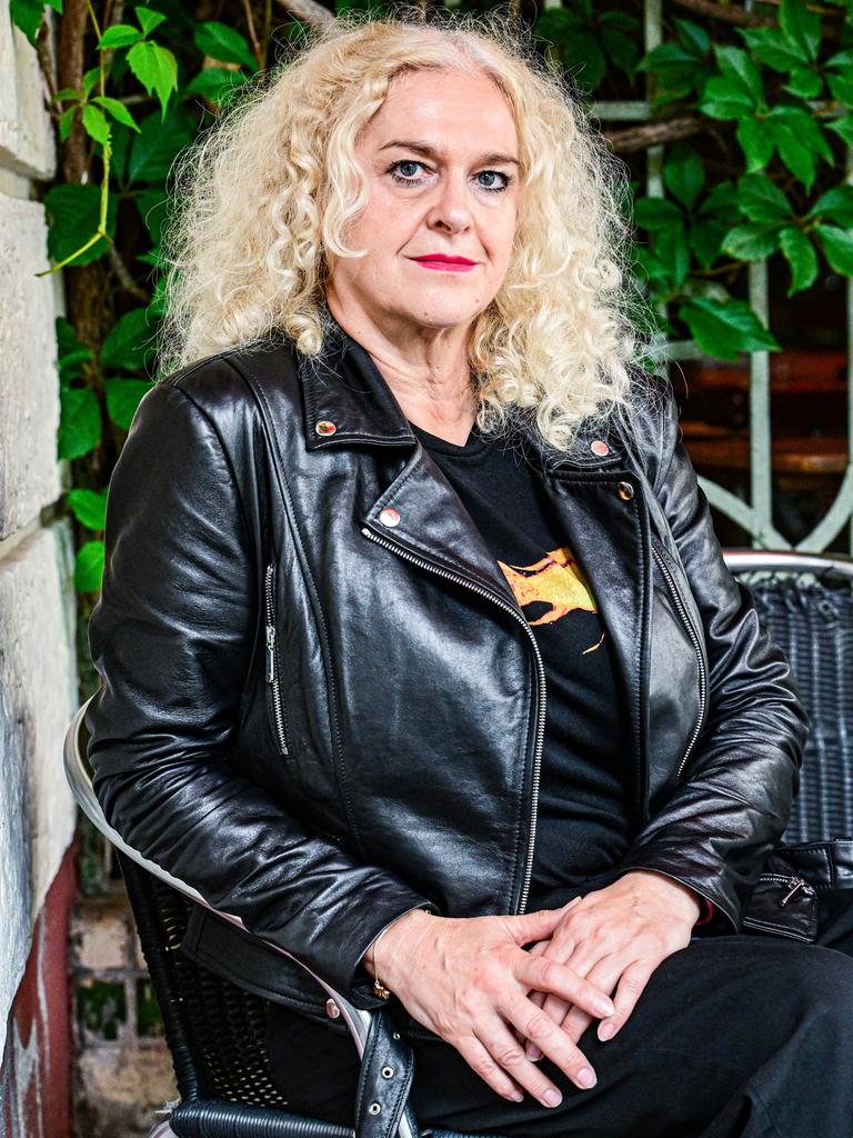 Vernesa Berbo posiert auf einem Stuhl sitzend für die Kamera. Sie trägt eine schwarze Lederjacke, roten Lippenstift und wilde blonde Locken.