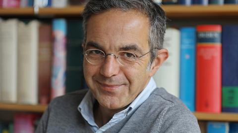 Navid Kermani sitzt lächelnd vor einem Bücherregal