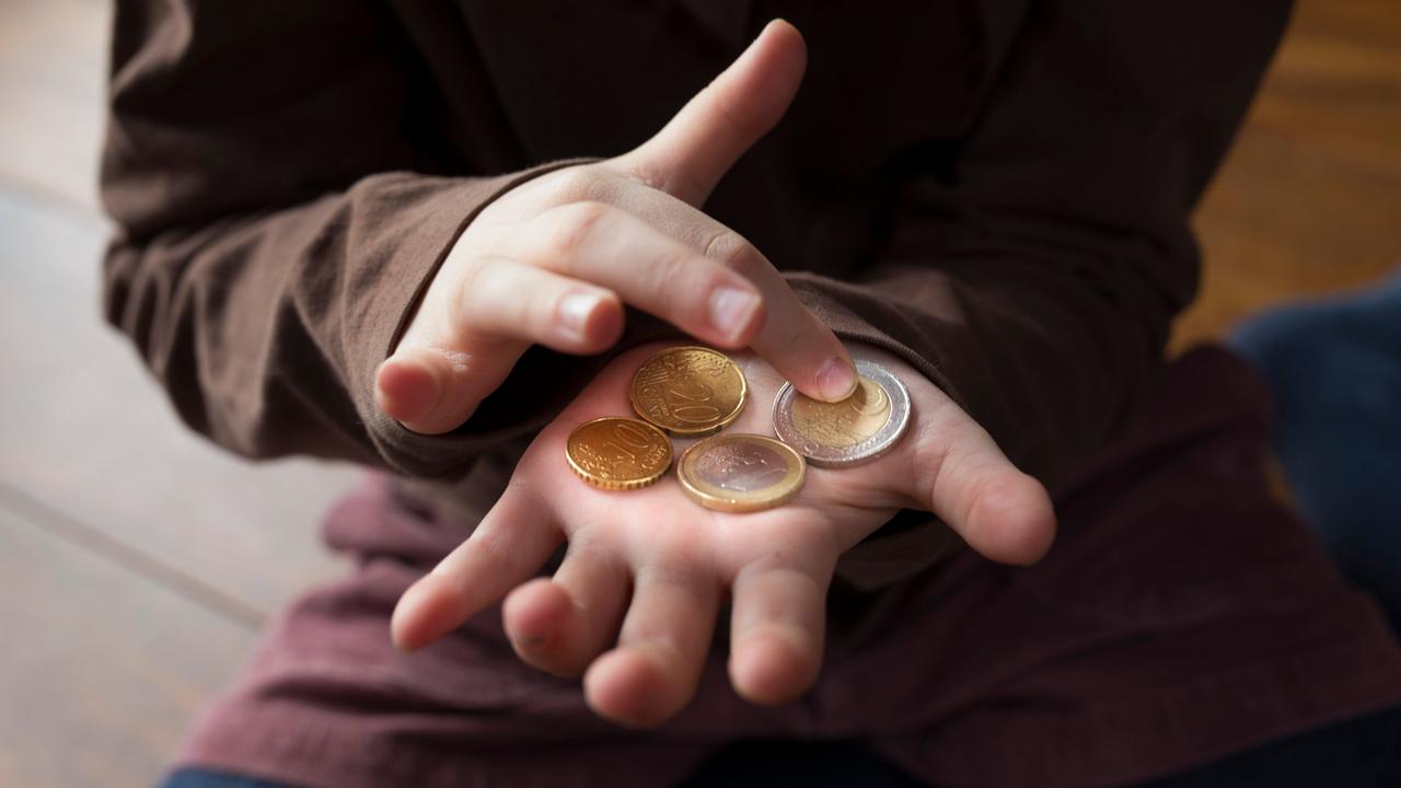 Ein Kind zählt kleines Taschengeld auf seiner Hand.